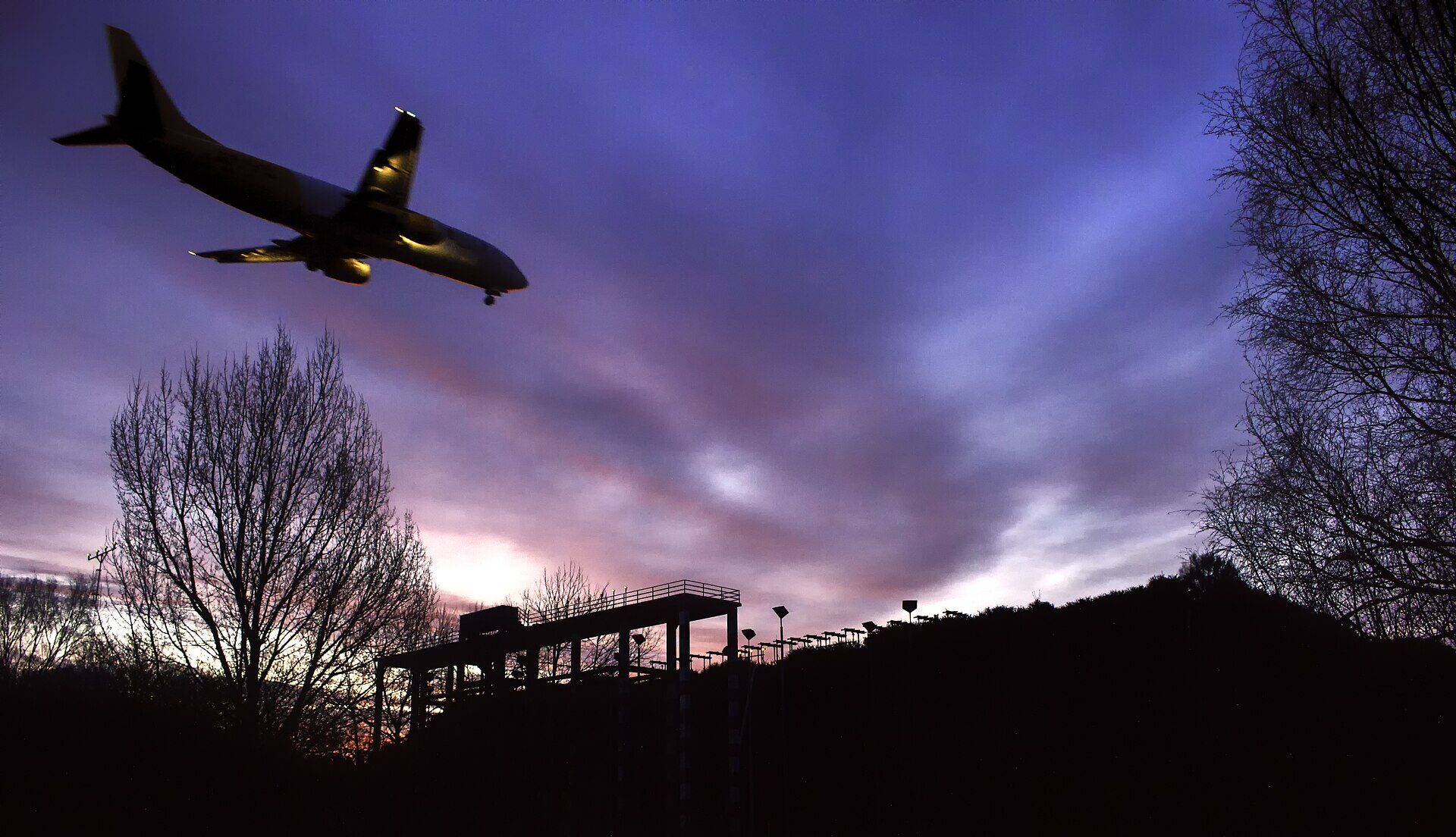 Boeing aircraft flying overhead into Santiago de Compostela airport, pink sunrise in the background.