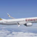 Ethiopian Airlines B737 flying under a blue sky on top of clouds. Ethiopian's logo is seen on the side of the aircraft, written in red.