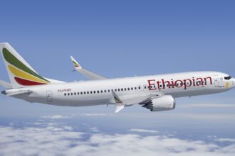 Ethiopian Airlines B737 flying under a blue sky on top of clouds. Ethiopian's logo is seen on the side of the aircraft, written in red.