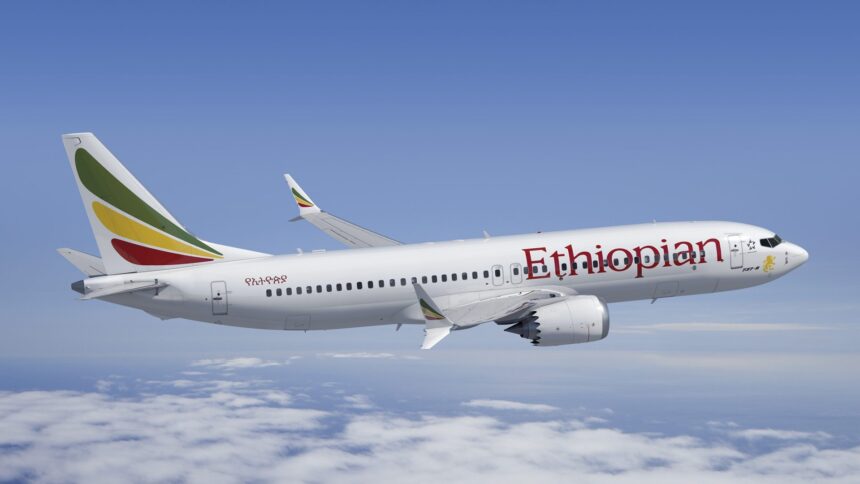 Ethiopian Airlines B737 flying under a blue sky on top of clouds. Ethiopian's logo is seen on the side of the aircraft, written in red.