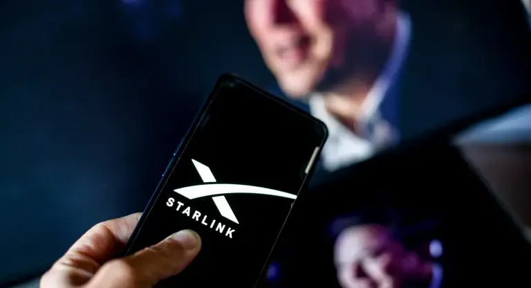 Starlink logo on a phone, with a blurry figure of a man in the background.