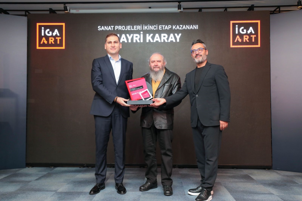 Hayri Karay was presented with the iGA Art Award by Istanbul Airport's Deputy CEO, all men standing in front of the iGA Art black panel.