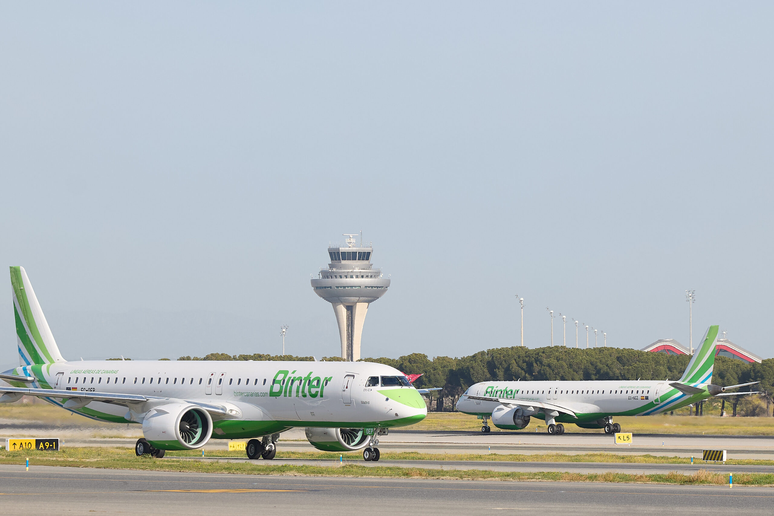 Two white and green Binter planes face each other on an airport runway.