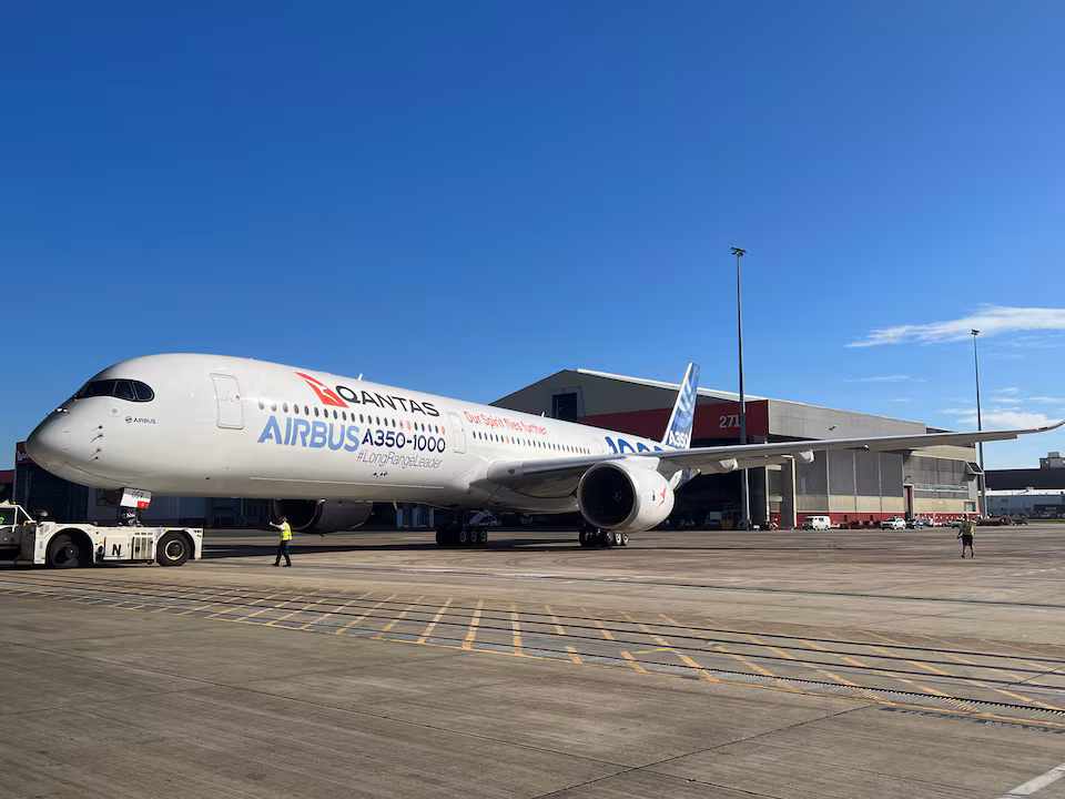 A Qantas aircraft stationed on the ground facing the camera, amid blue skies and grey ground.