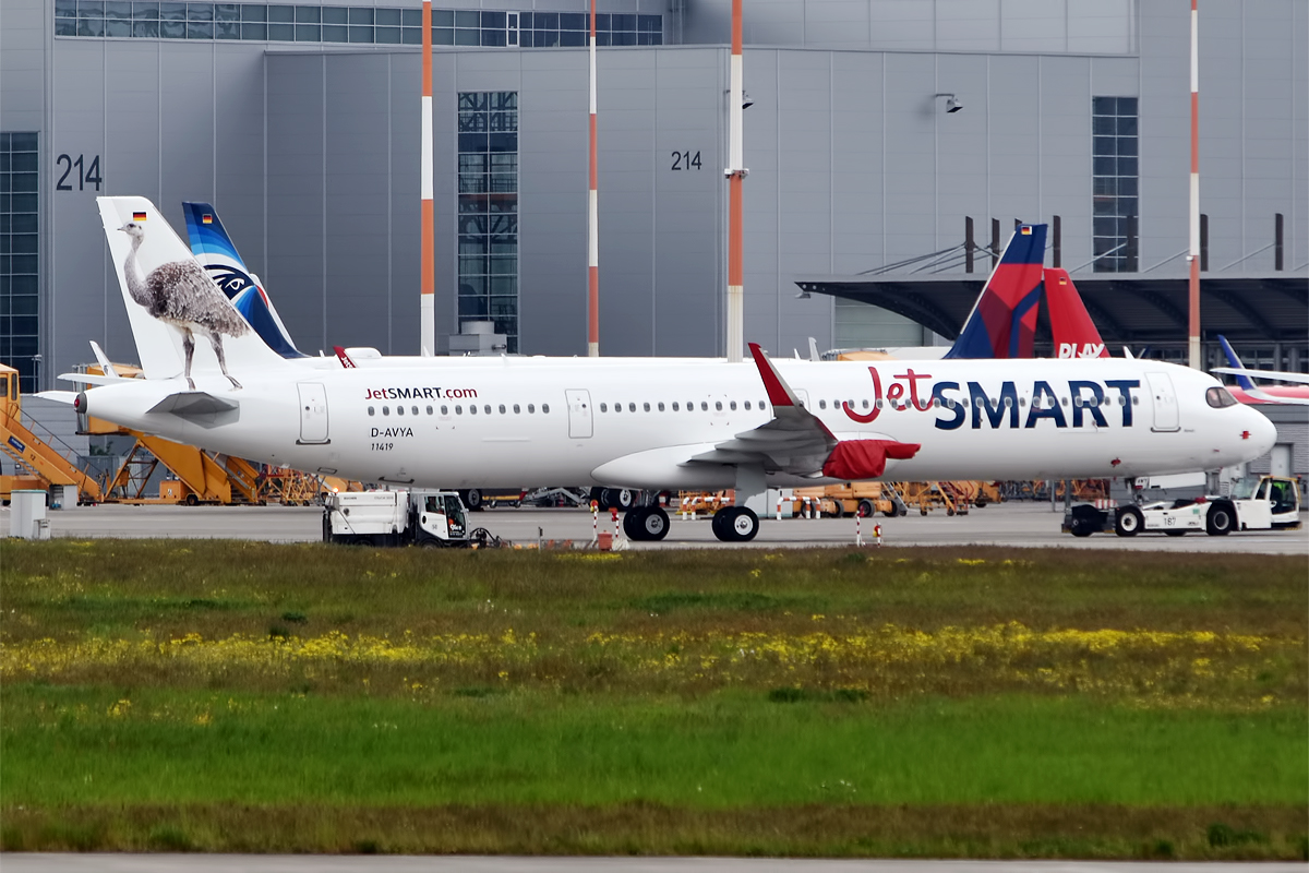 JetSMART, D-AVYA/CC-AWY, Airbus A321-271NX aircraft on the tarmac, grass in foreground.