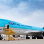 Korean Air aircraft pictured among blue skies with a few clouds and a yellow maintenance tool to the nose of the vehicle.