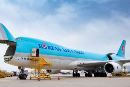 Korean Air aircraft pictured among blue skies with a few clouds and a yellow maintenance tool to the nose of the vehicle.