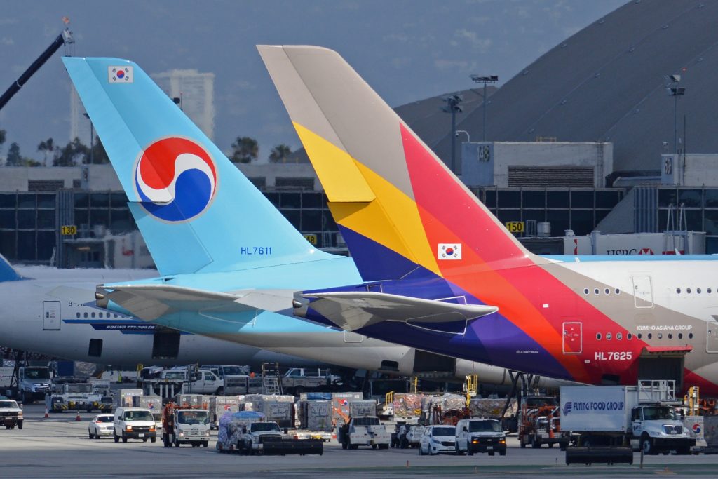 Image of Korean Air and Asiana Airlines aircrafts side by side with only the rear-end facing the camera. They are on the ground among other vehicles.