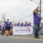 Merrie Monarch Parade, Hawaiian Airlines staff marching, holding a banner of their company, wearing purple shirts.