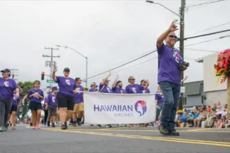 Merrie Monarch Parade, Hawaiian Airlines staff marching, holding a banner of their company, wearing purple shirts.