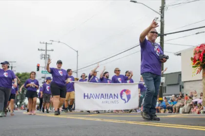 Merrie Monarch Parade, Hawaiian Airlines staff marching, holding a banner of their company, wearing purple shirts.