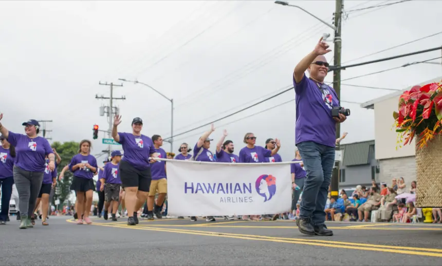 Merrie Monarch Parade, Hawaiian Airlines staff marching, holding a banner of their company, wearing purple shirts.