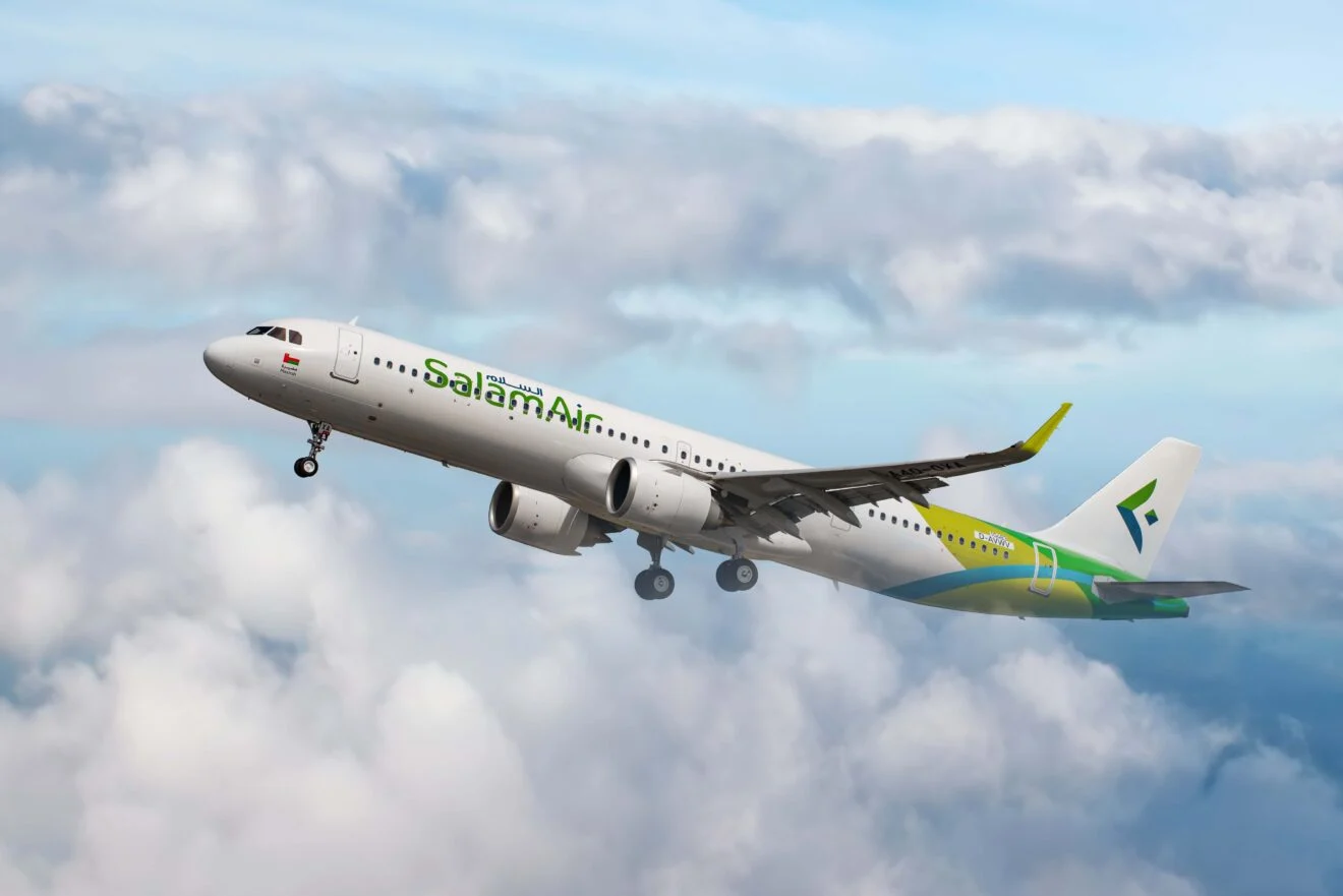 A SalamAir aircraft flying through clouds, between blue skies and grey clouds.