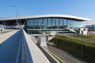 Exterior of Santiago de Compostela airport. Bushes on the right side, blue sky in the background.