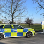 A police car sitting beside a stretch of grass with trees in the background