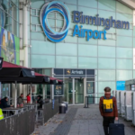 A man walking into a blue building with a large sign reading 'Birmingham Airport'