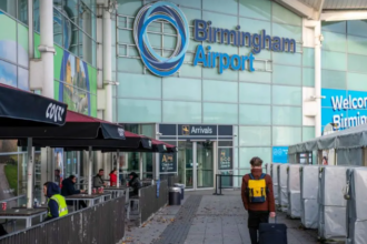 A man walking into a blue building with a large sign reading 'Birmingham Airport'