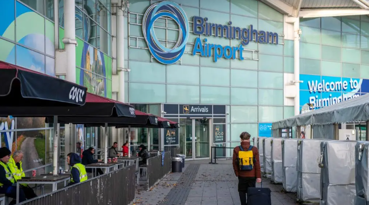 A man walking into a blue building with a large sign reading 'Birmingham Airport'