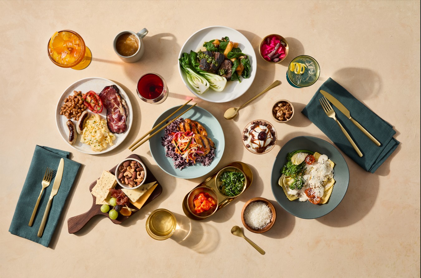 An overhead view of a neatly arranged table spread featuring a variety of colourful dishes and drinks on a light beige surface.
