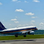 A large blue and white jetliner flying through a blue sky