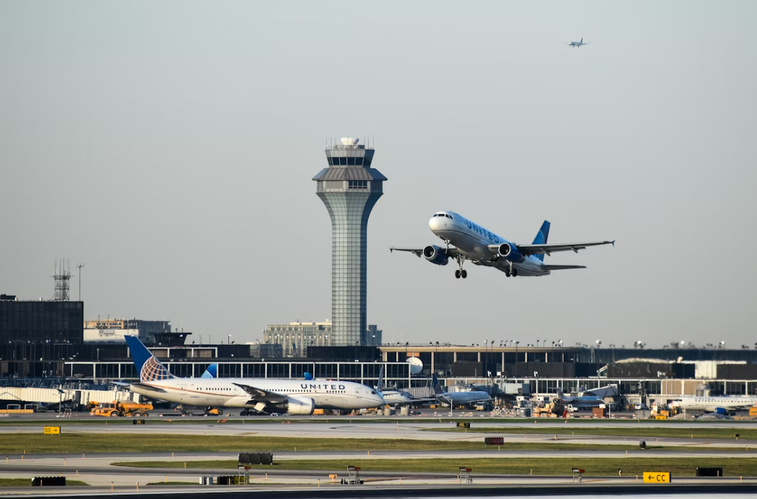 A white airplane taking off from an airport runway with a grey sky.