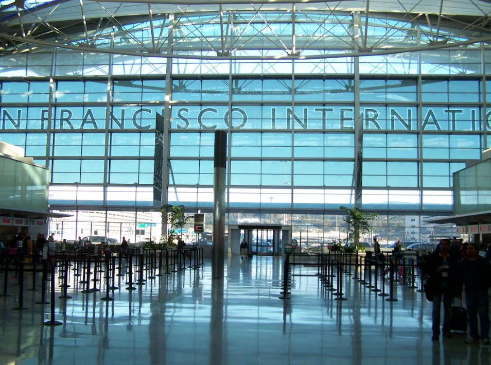 An airport entrance lobby with a giant glass window and blue sky outside