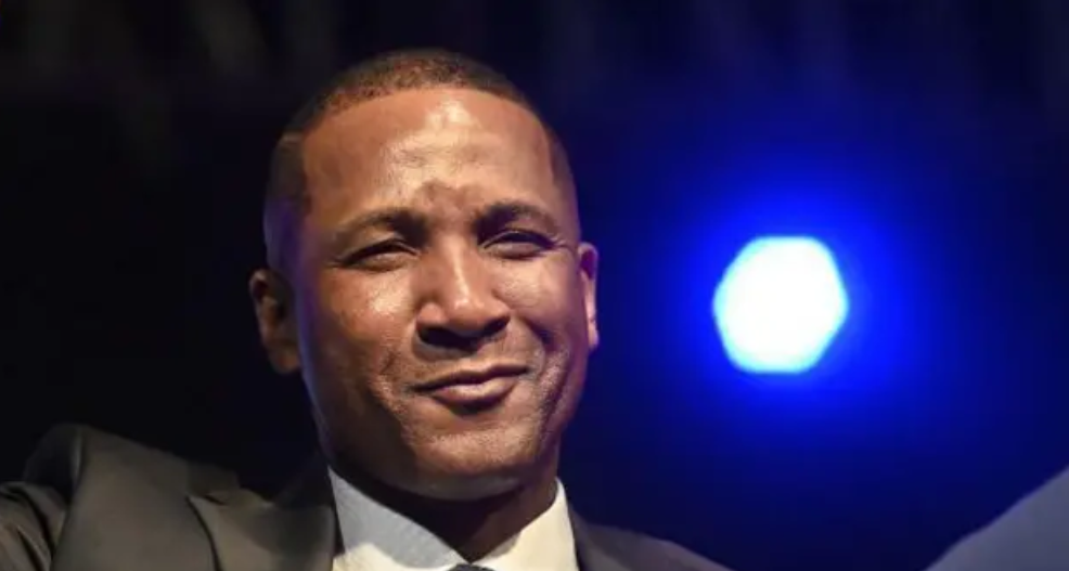 A man wearing a suit looking at the camera with a blue light in the background