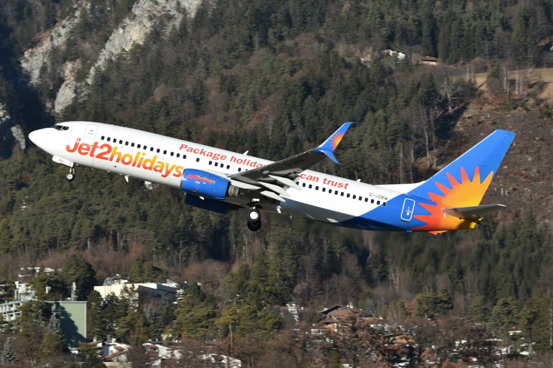 A large blue and white Jet2 Holidays plane taking off near mountains