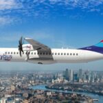 Skybus aircraft flying over a city, lake in the background, blue sky.
