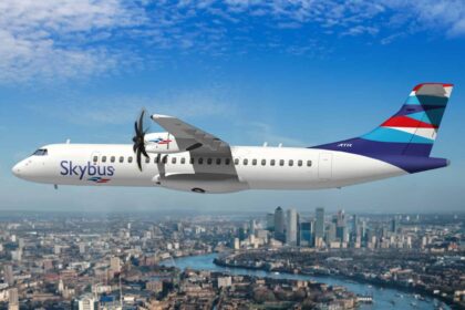Skybus aircraft flying over a city, lake in the background, blue sky.