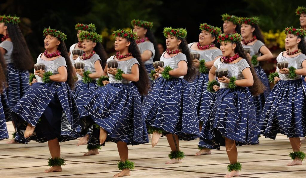 Hālau Nā Lei Kaumaka O Uka, women in grey shirts and blue dresses dancing inside, holding coconuts. 