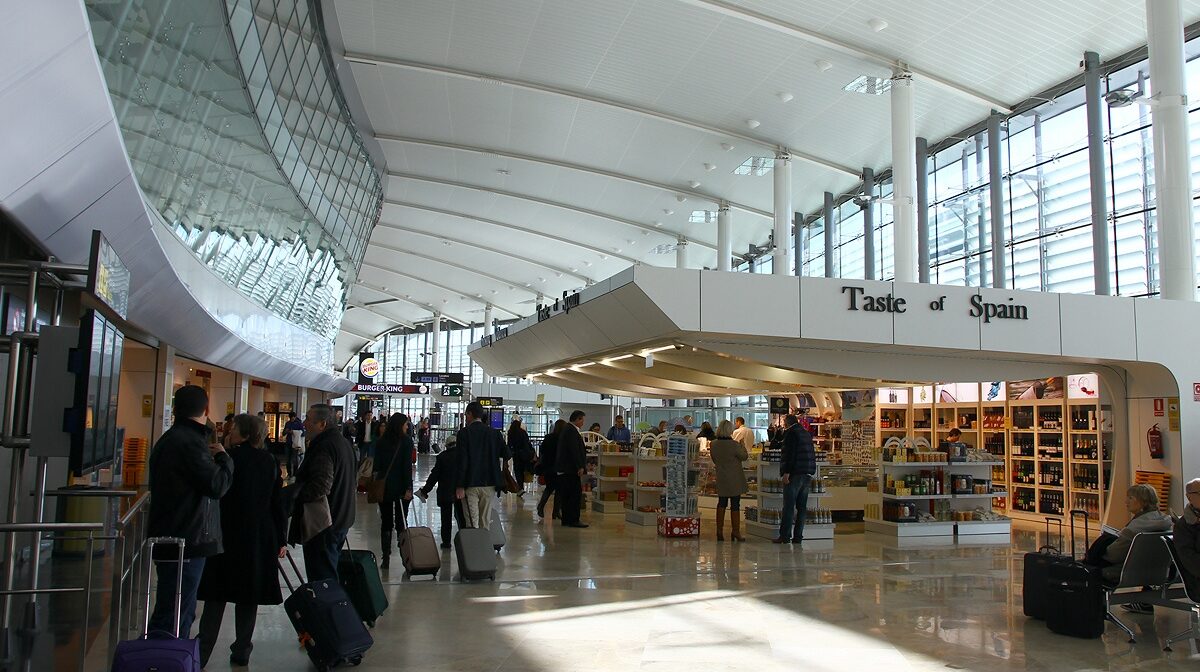 Interior of Valencia Airport, people with suitcases and a shop that says "Taste of Spain".
