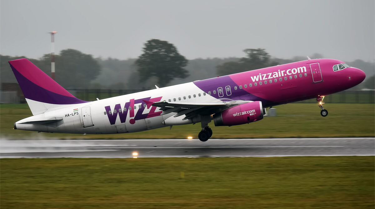 Wizz Air Airbus aircraft taking off from London Luton Airport. Grass in foreground, trees in background.