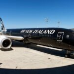 Air New Zealand Boeing 787-9 Dreamliner facing the camera with a black and white exterior, on the ground and next to a building.
