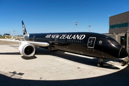 Air New Zealand Boeing 787-9 Dreamliner facing the camera with a black and white exterior, on the ground and next to a building.