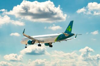 Aer lingus aircraft in a clear light blue sky with some clouds.