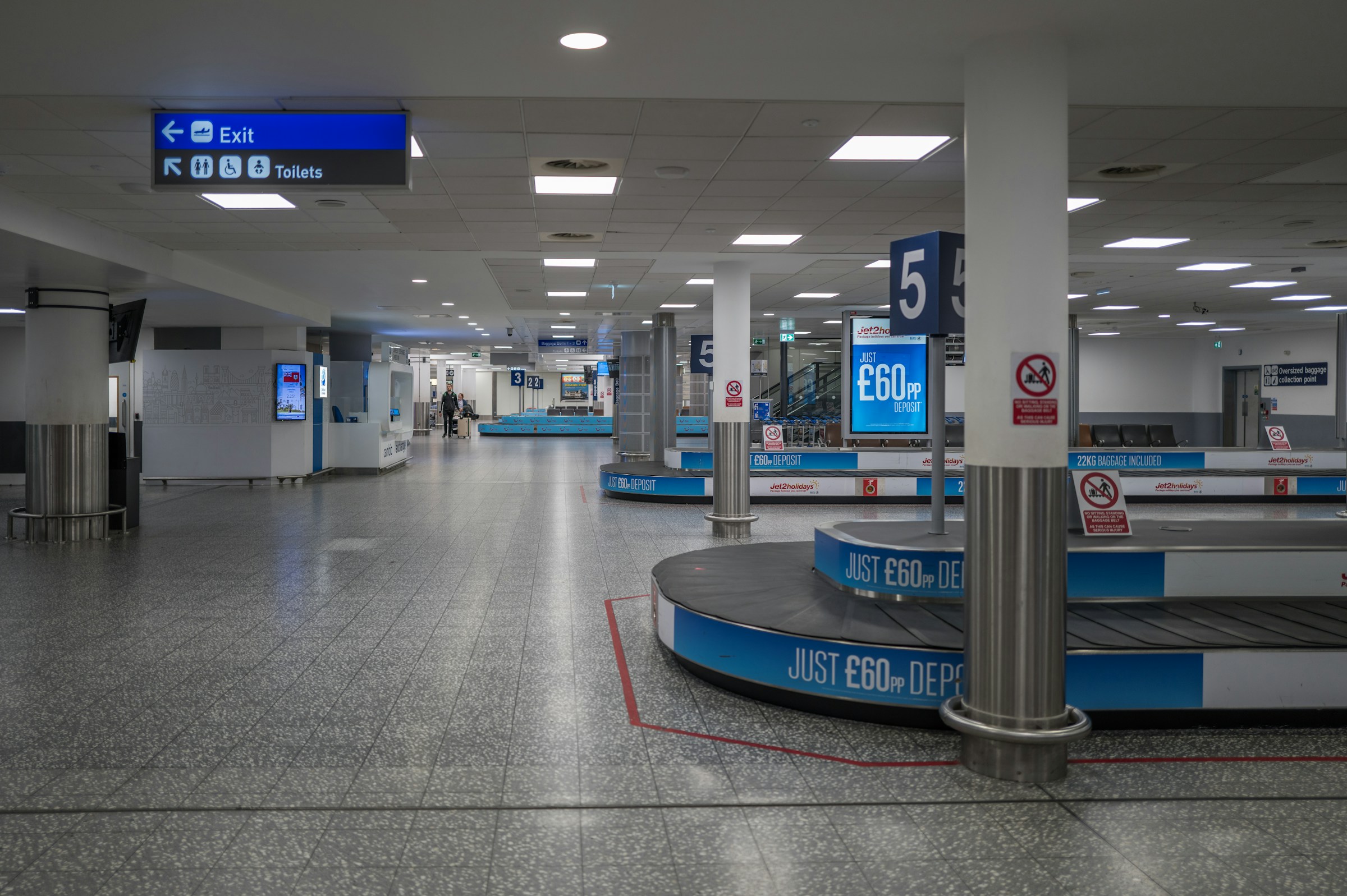Baggage claim area at Bristol Airport, signs indicating exit and toilet direction. 