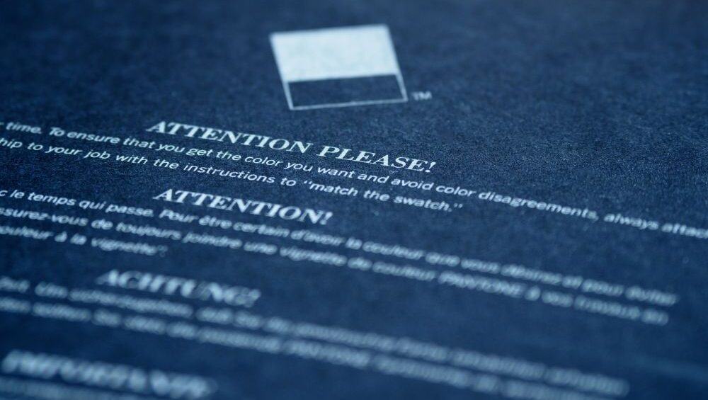 A generic image of a charcoal grey coloured 'attention please!' notice sign. Attention is translated into multiple languages going down the page, blurring out at the bottom.