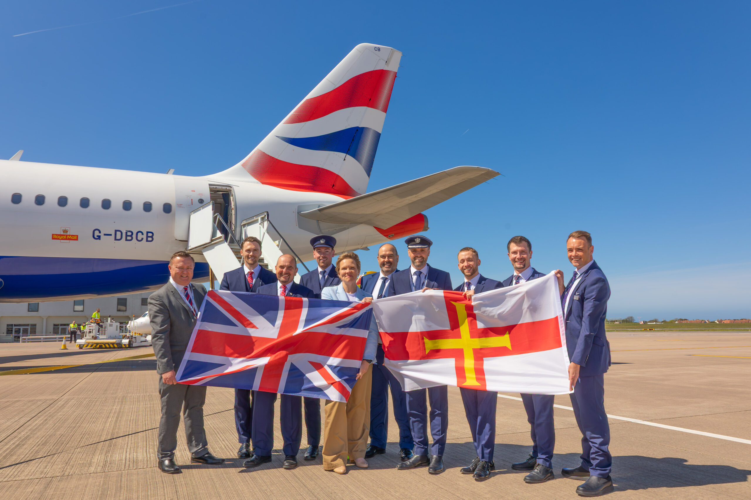 British Airways crew hold the national flag of the UK and the flag of Guernsey flags to celebrate the inaugural flight to Guernsey