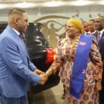 A man and a woman shaking hands with a black car in the background