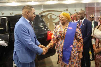 A man and a woman shaking hands with a black car in the background