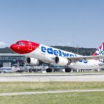 A Edelweiss Airbus A320 taking off; airport terminal in the background.