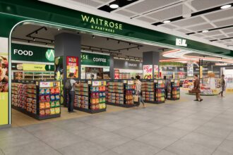 The image shows a dual branded Waitrose-Relay shop inside London Heathrow Airport Terminal 2. Along the top of the image is the dual branded logo in forest green and white. A range of colourful displays can be seen on stalls and shelves in the shop.