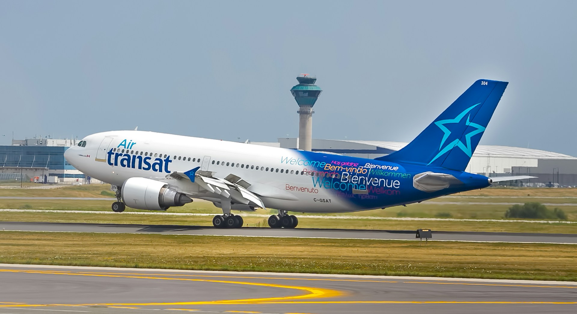 Air Transat aircraft landing, white and blue livery. Buildings in the background and against a grey sky.