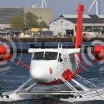 A DHC-6-300 aircraft being in operation at Copenhagen Seaport. Gliding on the water, buildings in the background.