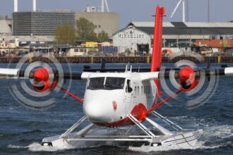 A DHC-6-300 aircraft being in operation at Copenhagen Seaport. Gliding on the water, buildings in the background.