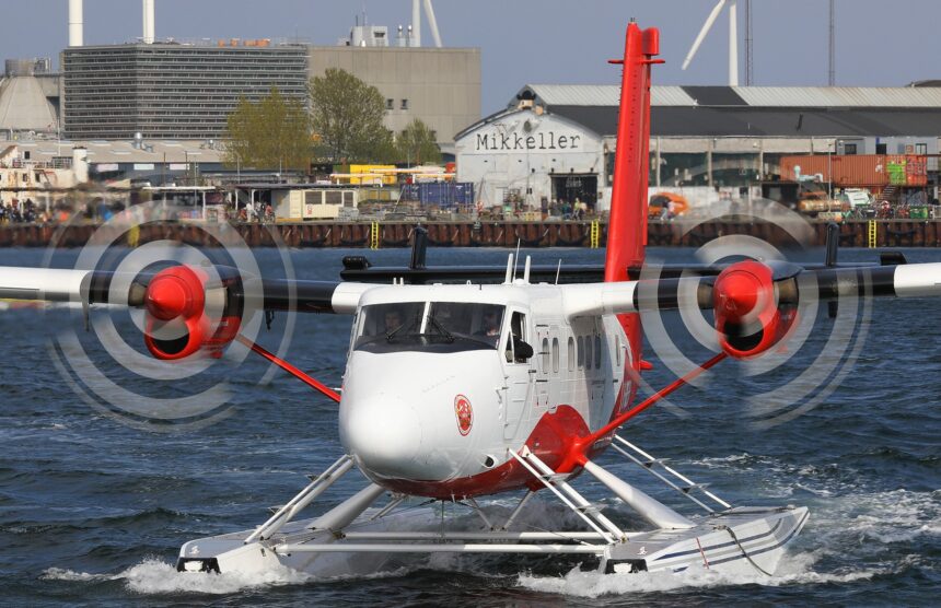 A DHC-6-300 aircraft being in operation at Copenhagen Seaport. Gliding on the water, buildings in the background.