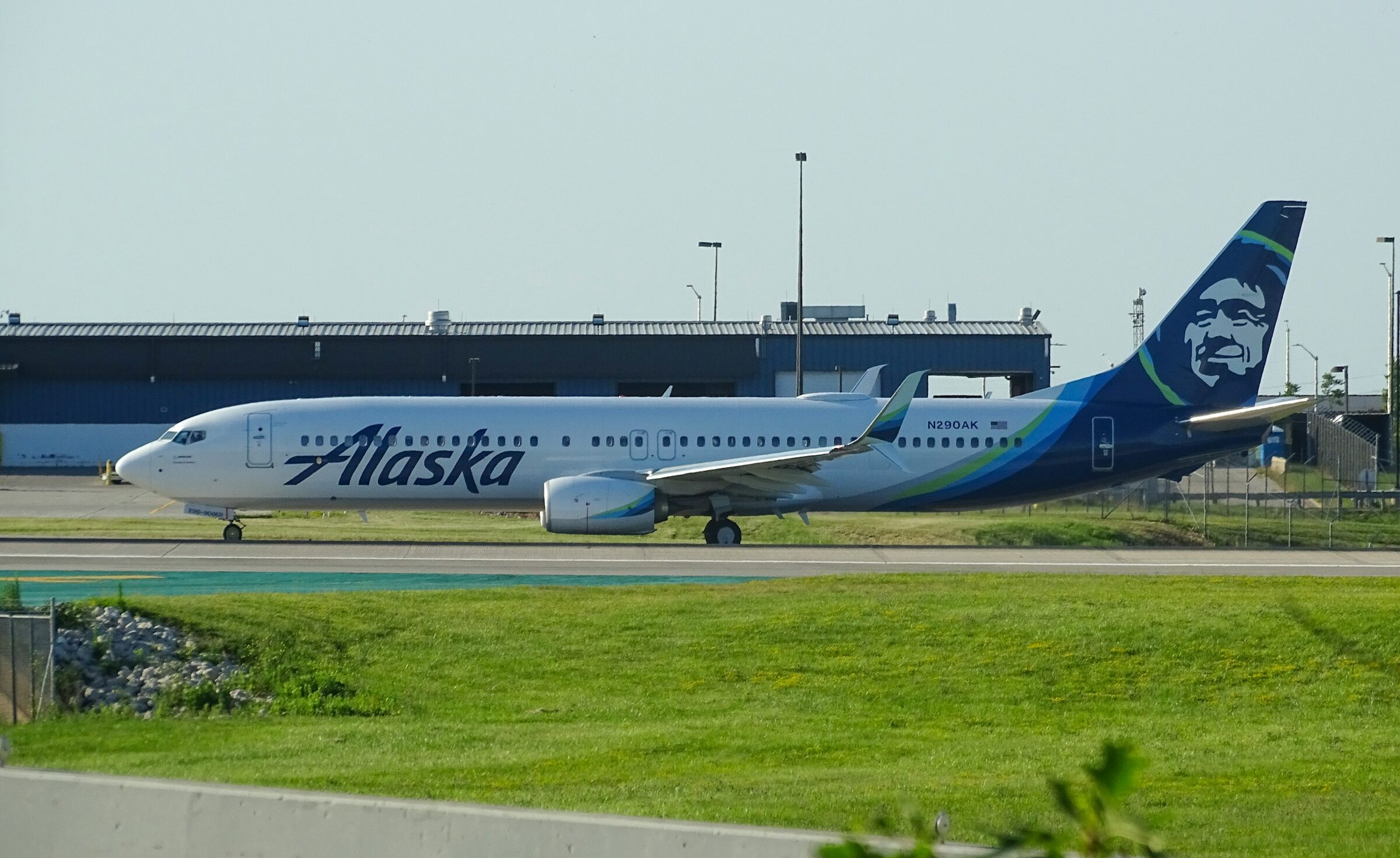 Alaska Airlines aircraft on the tarmac before takeoff, grass in the foreground.