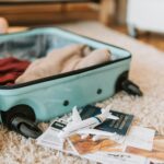 Turquoise open suitcase laying on a cream carpet with a passport and a toy plane next to it