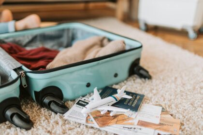 Turquoise open suitcase laying on a cream carpet with a passport and a toy plane next to it